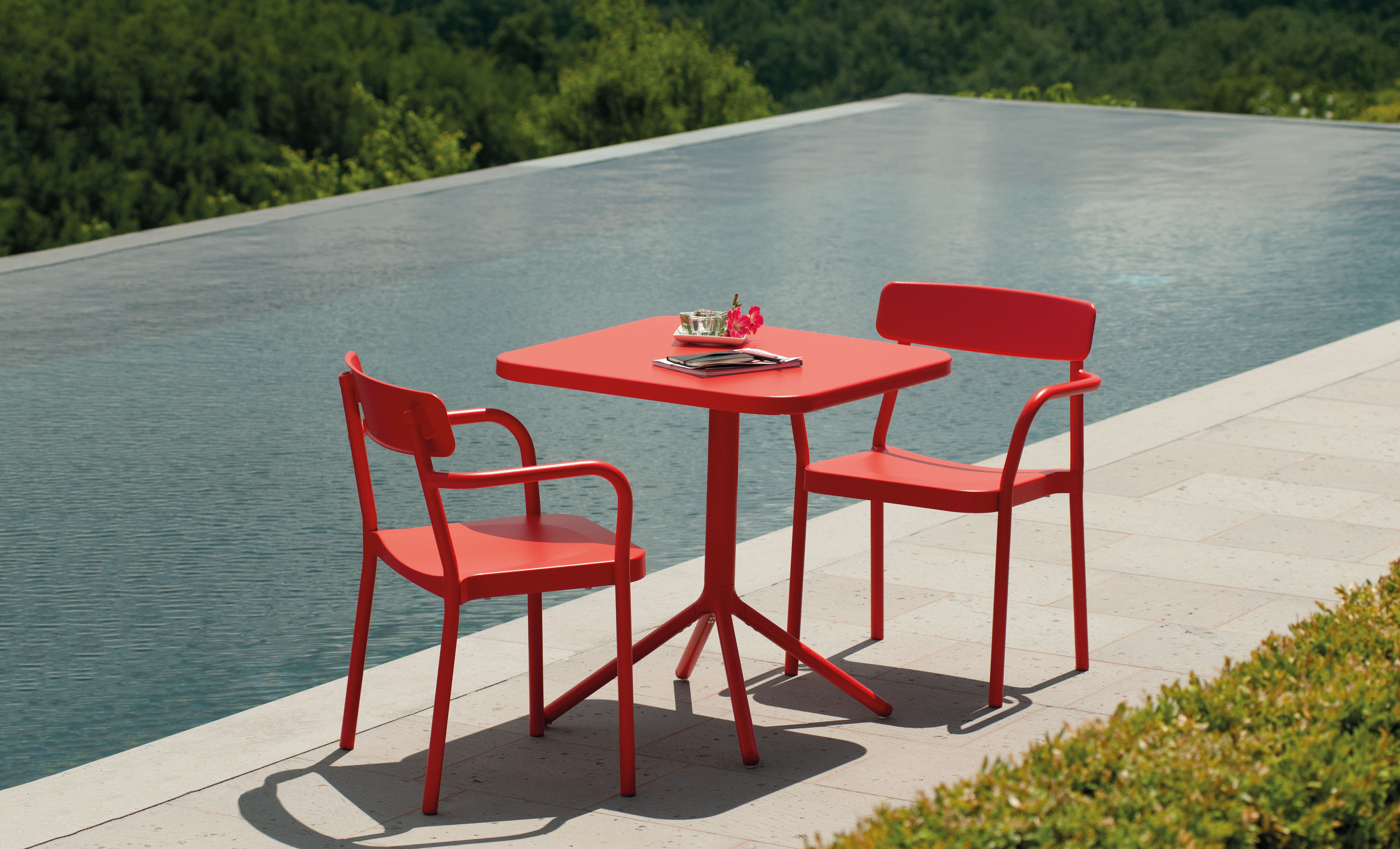Emu Grace chairs and table in coral red beside an infinity pool, no people