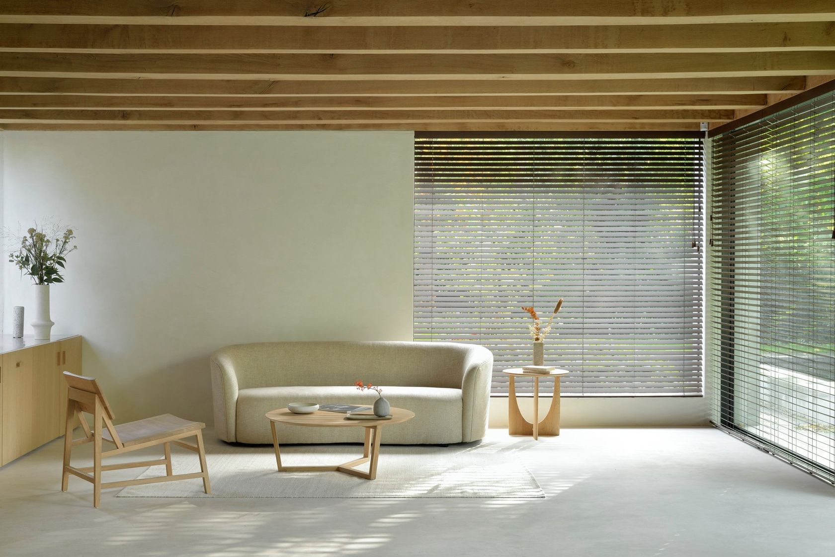 An Ethnicraft living room with the oatmeal Ellipse sofa, wooden ceiling beams and a low coffee table, no people