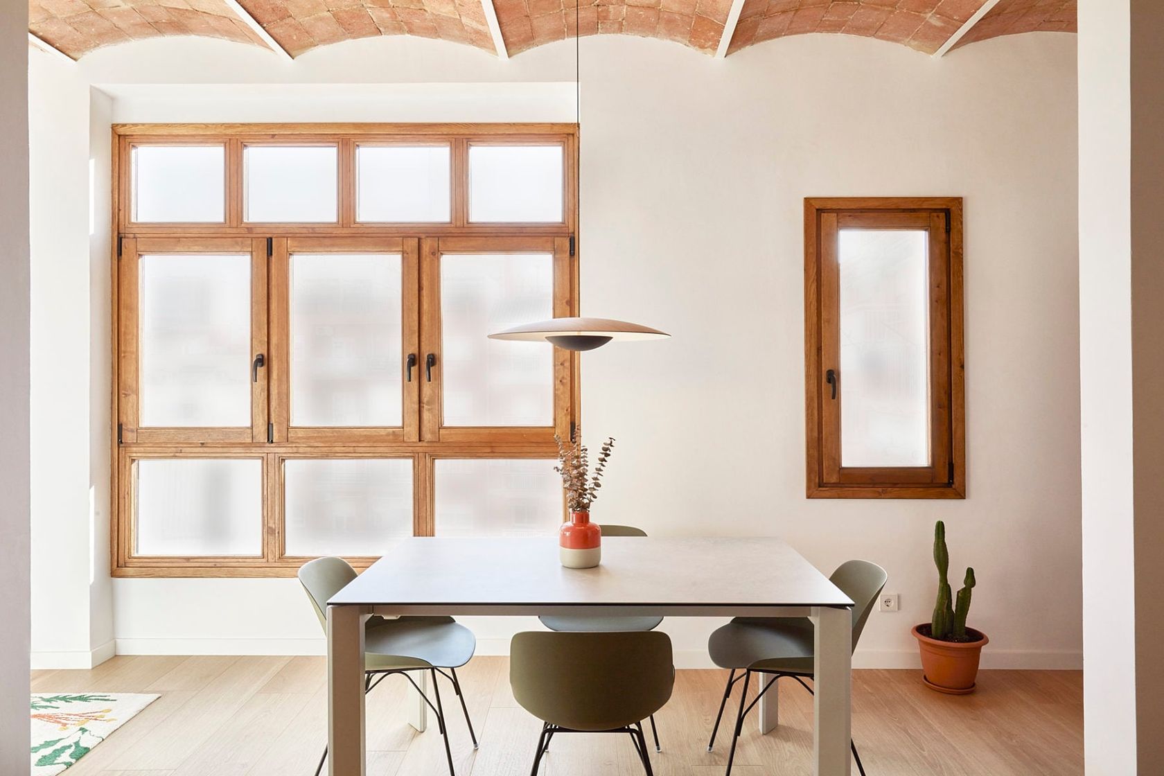 A Marset Ginger pendant lit above a dining table in a bright Barcelona apartment with a vaulted brick ceiling, no people