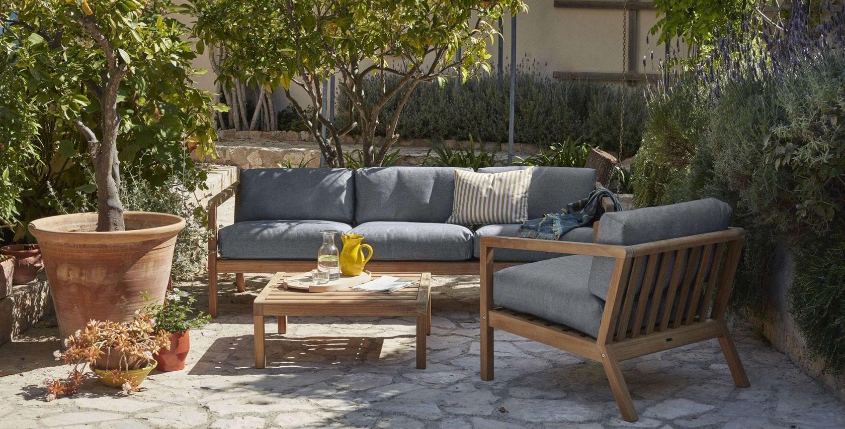 Skagerak teak outdoor sofa and lounge chairs arranged in a Mediterranean courtyard garden, no people