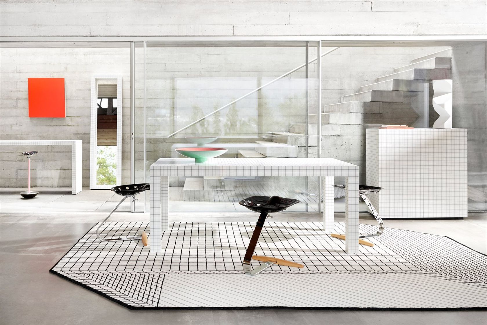 A Zanotta interior with the Quaderna grid table and Mezzadro stools on a matching grid rug in a concrete room, no people